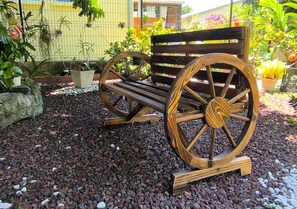 A wooden bench with large wheels, placed on gravel, surrounded by plants and a fence. - New Listing (Saint-André)