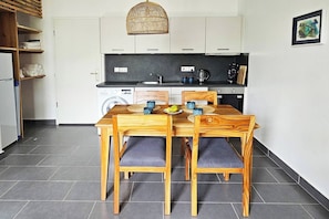 A compact kitchen with a dining area, featuring a wooden table and chairs, a washing machine, and a hanging light fixture. - Flat "Zanzi Dream" at The Soul with Pool, balcony, AC (Paje)