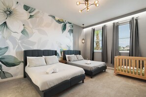 Une chambre avec deux lits, un berceau, une grande fresque murale à motifs floraux et un lustre moderne.