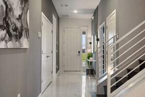 A hallway with a white door, a staircase with a metal railing, and a wall with a large abstract painting. - Near Disney/Theater & Game Rooms/Private SPA 25140 (Kissimmee)