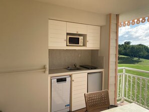 A kitchenette with a microwave, a sink, and a small refrigerator. There is a chair and a table with a view of a green landscape. - New Listing (Sainte-Luce)