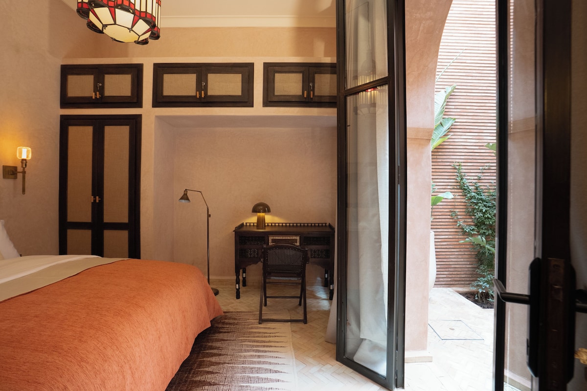 A bedroom with a bed, a desk, a chair, and a large window.