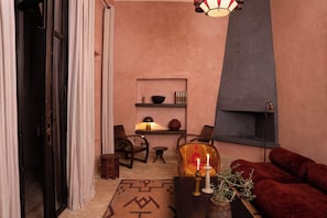 A cozy living room with a fireplace, a red sofa, a wooden coffee table, and a patterned rug. - Dar Al Qamar (Marrakech)