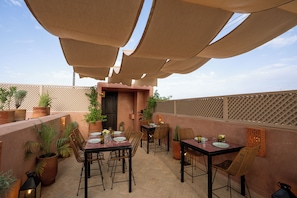 An outdoor dining area with tables and chairs, surrounded by potted plants and a wooden fence. - Dar Al Qamar (Marrakech)
