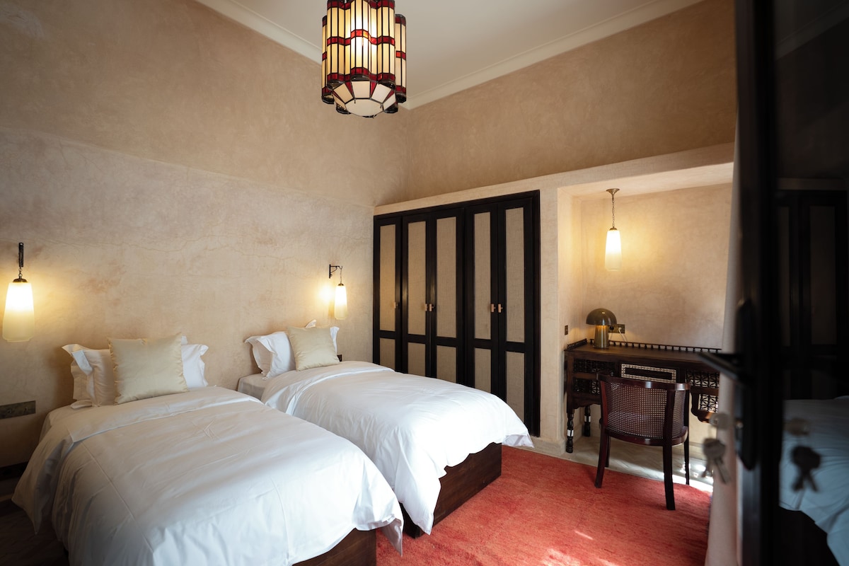 A hotel room with two beds, a desk, and a wardrobe.