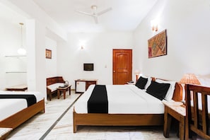 Ein Hotelzimmer mit einem großen Bett, einem Schreibtisch, einem Sessel, einem kleinen Kühlschrank, einem Nachttisch aus Holz und einem Deckenventilator.