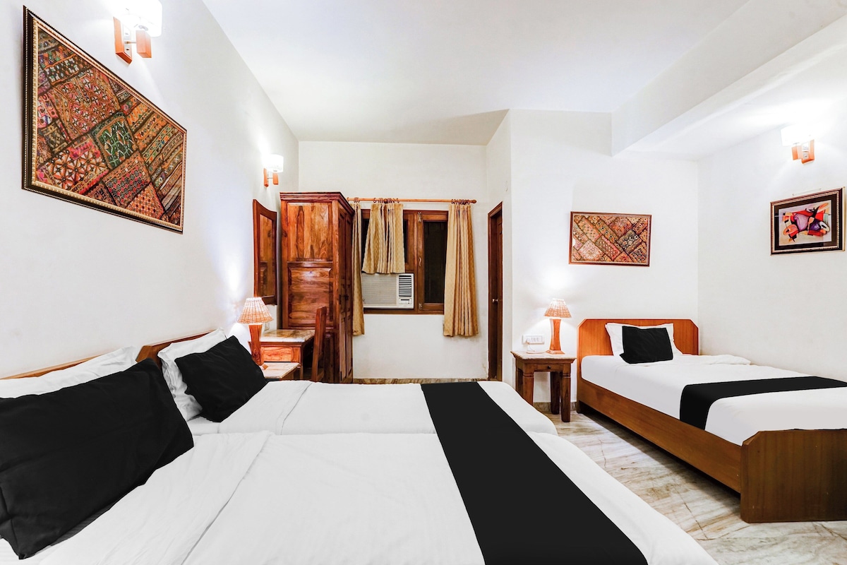 Ein Hotelzimmer mit zwei Betten, einem Holzschrank, einem kleinen Tisch mit Lampe und einem Fenster mit Vorhängen.