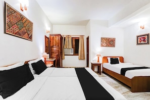 Ein Hotelzimmer mit zwei Betten, einem Holzschrank, einem kleinen Tisch mit Lampe und einem Fenster mit Vorhängen.