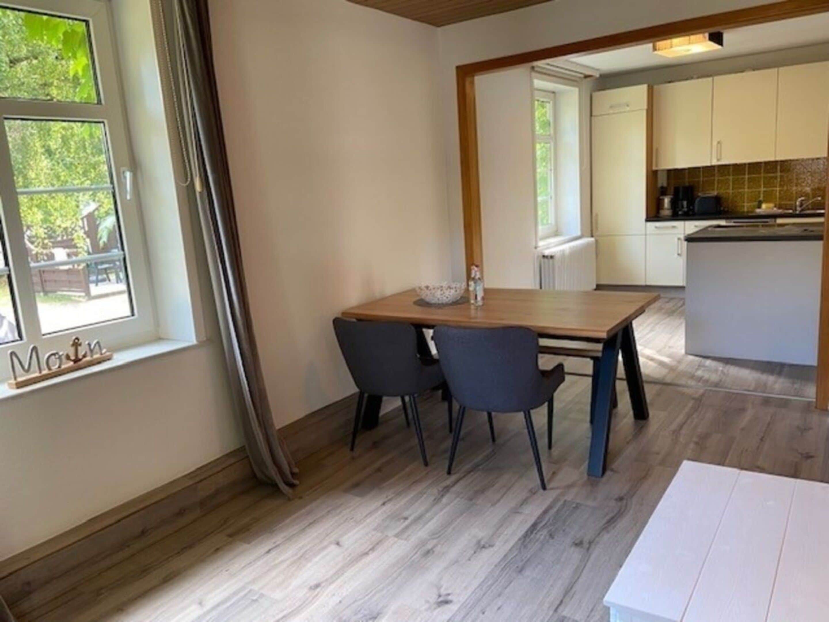 Een eetgedeelte met een houten tafel, twee stoelen en een raam met gordijnen.