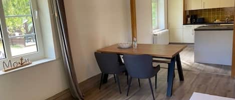 Een eetgedeelte met een houten tafel, twee stoelen en een raam met gordijnen.