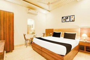 A hotel room with a large bed, a wooden headboard, a desk with a chair, a bedside table with a lamp, and a wall-mounted air conditioner. - Super Hotel O by OYO Chandigarh Road (Zirakpur)