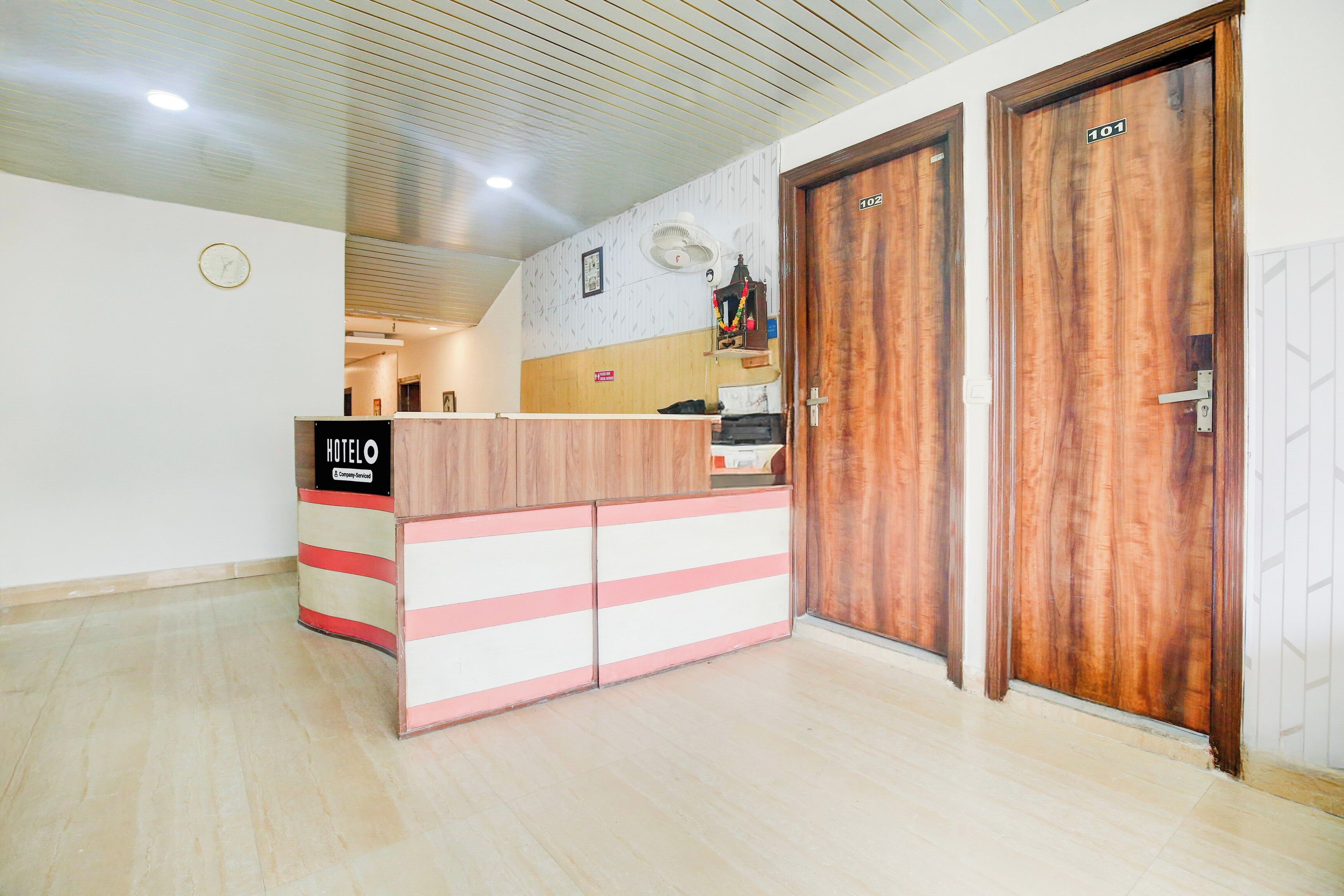 Un mostrador de recepción con un letrero que indica que es un hotel de servicio de empresa. Hay dos puertas de madera con los números 101 y 102.