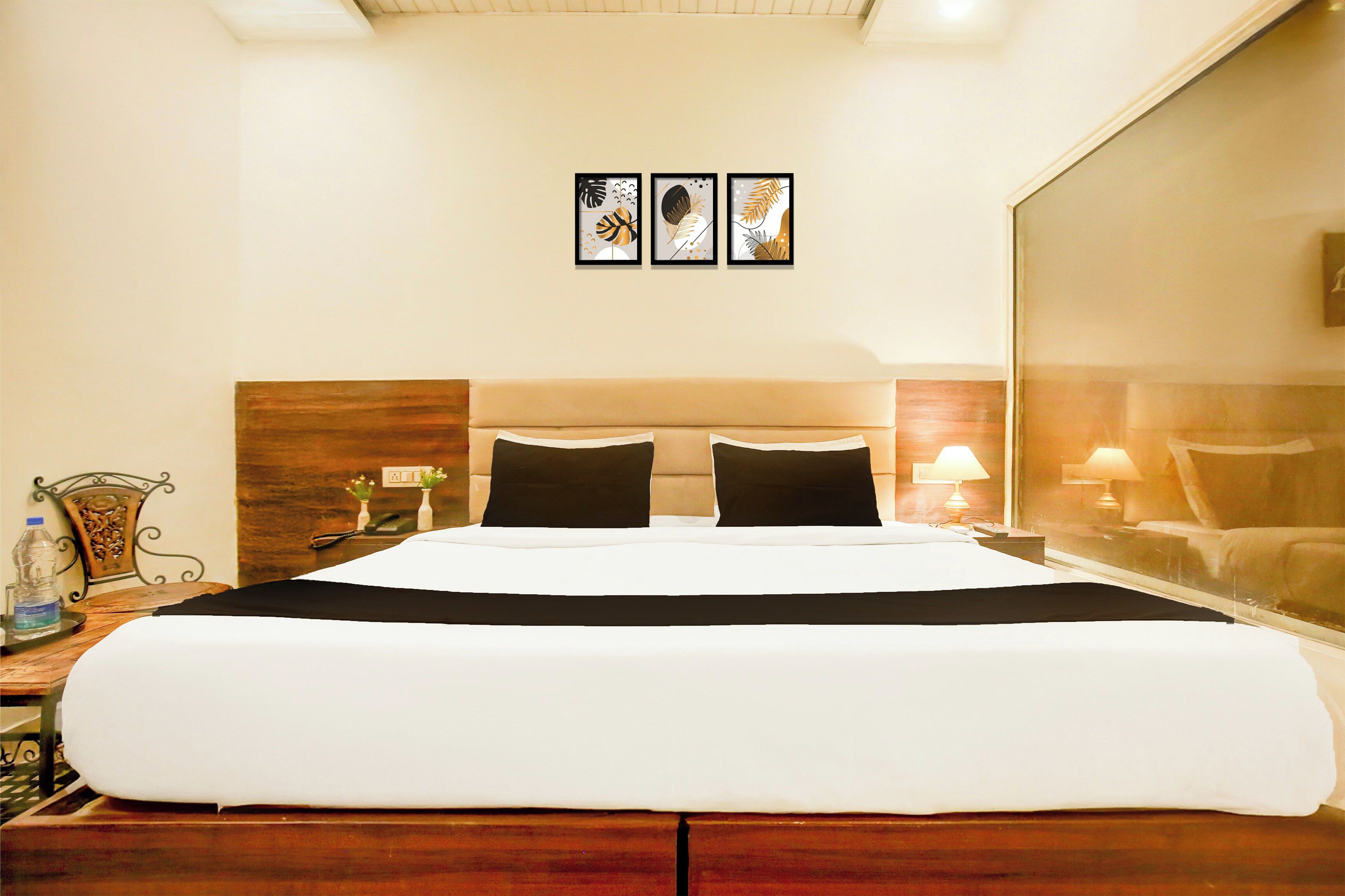 Habitación de hotel con una cama grande, dos mesitas de noche, un espejo y tres obras de arte enmarcadas en la pared.