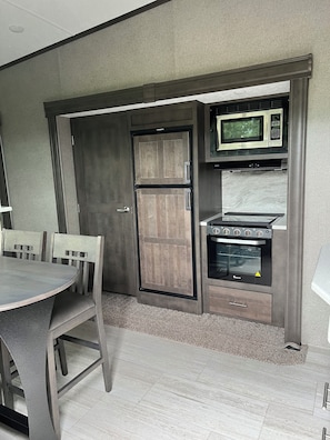Une cuisine compacte équipée d’un four à micro-ondes, d’un four traditionnel et d’un meuble en bois.