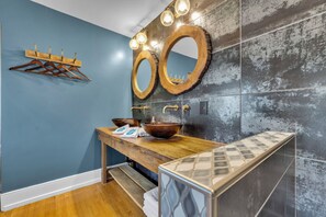 Une salle de bain avec un meuble-lavabo en bois, deux miroirs ronds, un lavabo sur colonne et un porte-serviettes.