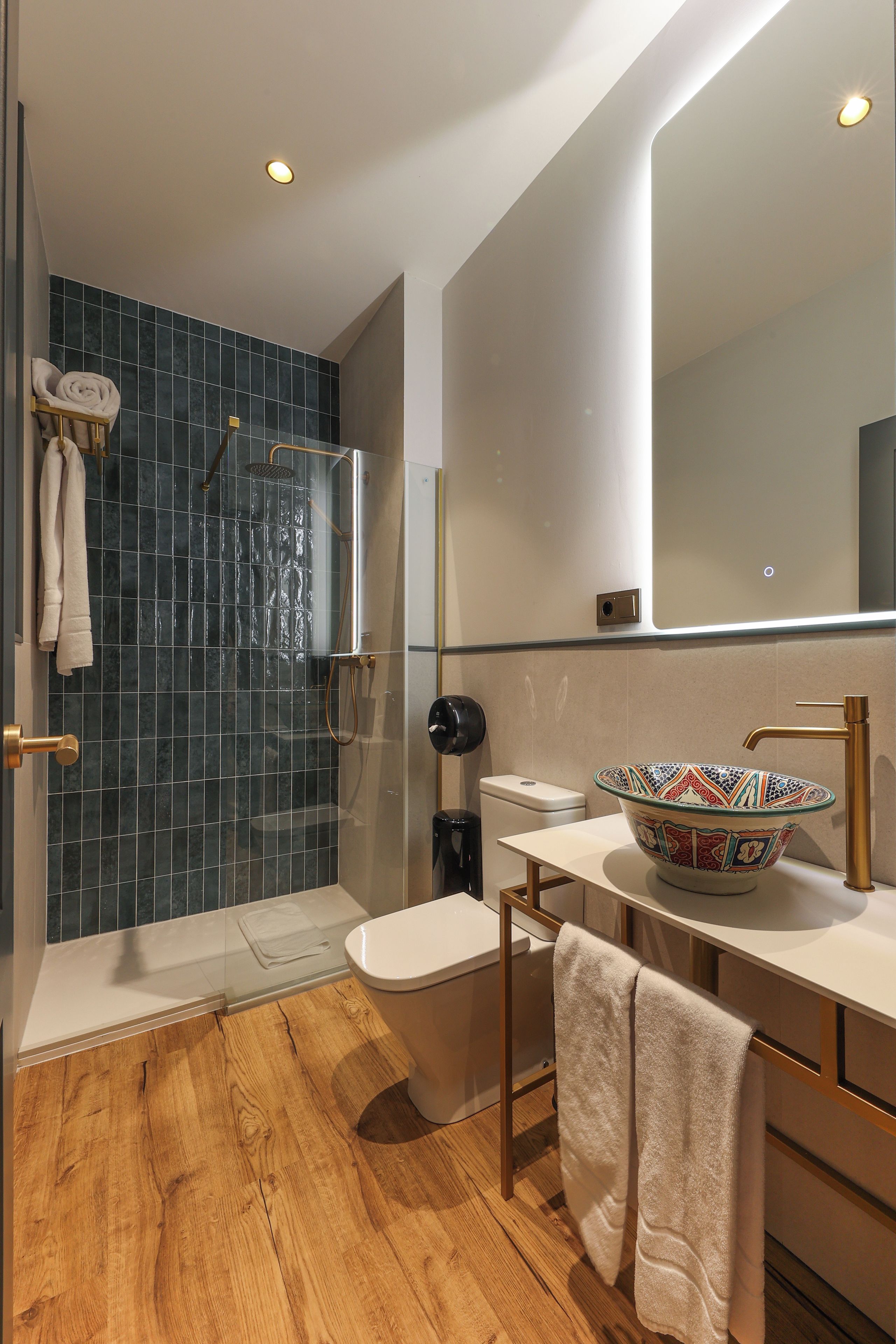 A modern bathroom with a glass-enclosed shower, a large mirror, and a wooden floor.