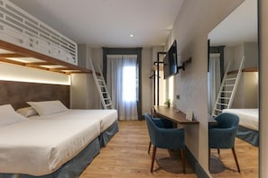 Habitación de hotel con una litera, un escritorio con dos sillas, un televisor montado en la pared y una ventana con cortinas.