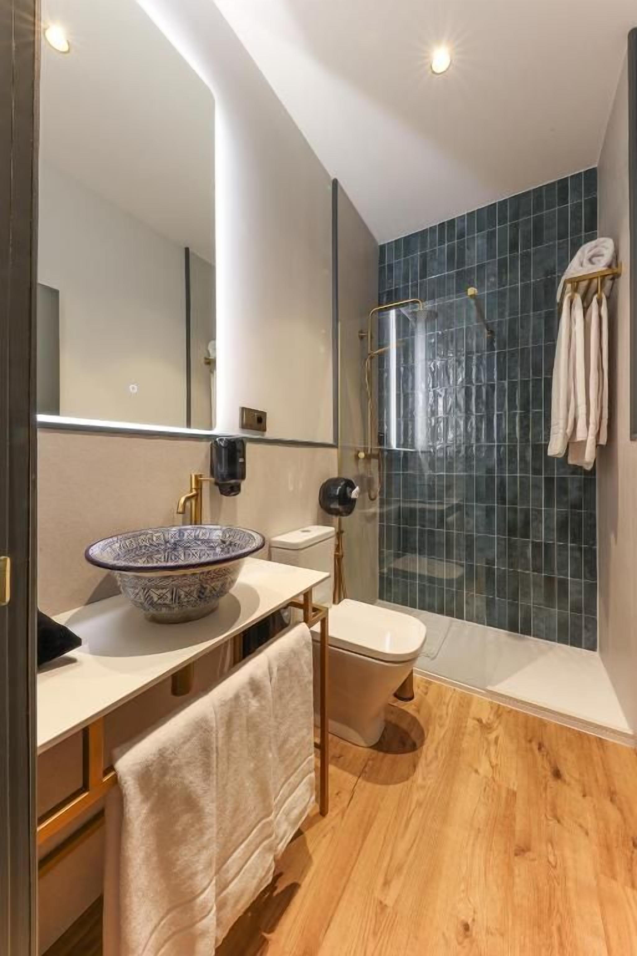 Un baño moderno con un espejo grande, un lavabo sobre encimera, un inodoro y una zona de ducha.