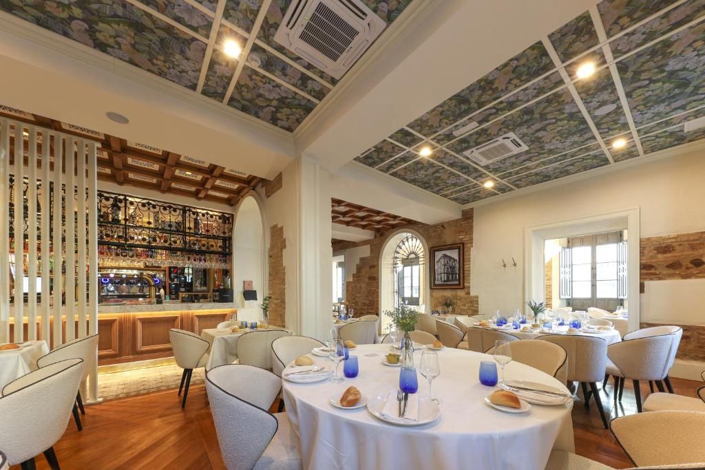 Un restaurante con mesas redondas, una zona de bar y un techo decorativo.