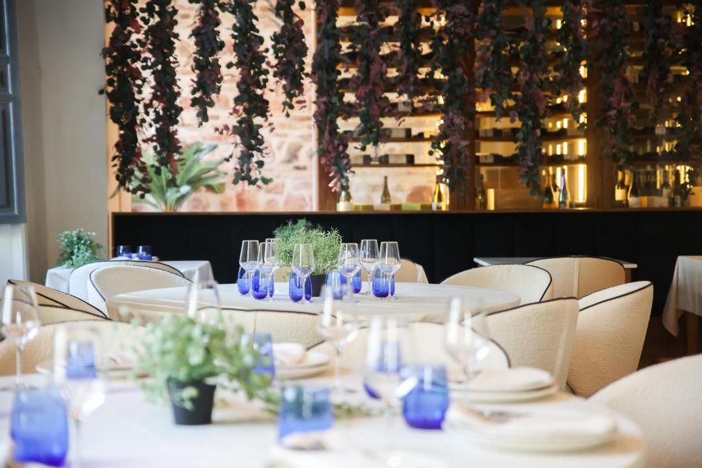A restaurant with round tables set for dining, featuring blue glassware and potted plants.
