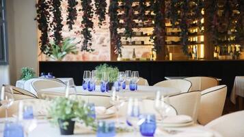 A restaurant with round tables set for dining, featuring blue glassware and potted plants.