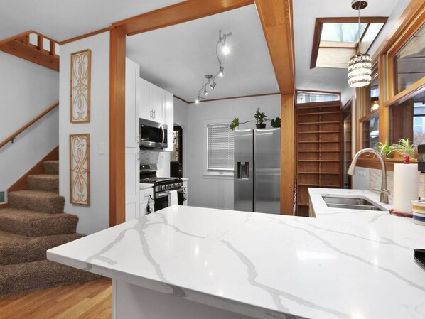 A kitchen with a marble countertop, stainless steel appliances, and a wooden staircase.