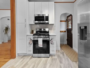 A modern kitchen with white cabinetry, stainless steel appliances, and a wooden floor. - A Stone's Throw | Steps to Lake Michigan (Gary)