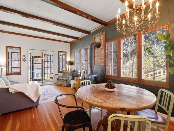 A cozy living room with a fireplace, wooden beams, and a dining area with a round table.