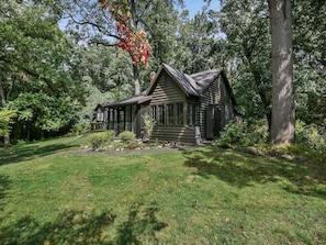 A log cabin with a front porch, surrounded by a well-maintained lawn and trees.