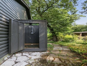 An outdoor shower area with a metal enclosure, a stone pathway, and a tree in the background.