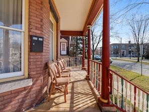 A brick building with a porch, numbered 906 9018, featuring wicker chairs and a red railing. - Blarney Downtown Penthouse & Private Yard (Michigan City)