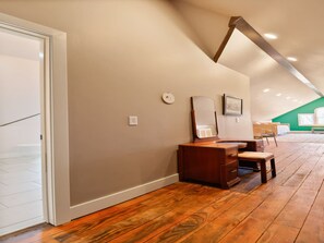 Ein Zimmer mit Holzboden, einem Schreibtisch mit Schubladen, einem Stuhl, einem Spiegel und einer grünen Wand im Hintergrund.