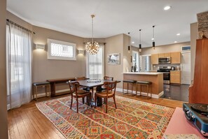 A modern kitchen with a central island, a dining area with a patterned rug, and a chandelier. - Blarney Bungalow | Renovated Downtown Charmer (Michigan City)