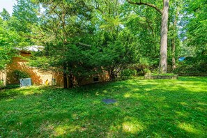 Ein Garten mit einem Ziegelhaus, einem großen Baum und einem Rasen.