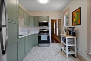 A kitchen with green cabinets, a microwave, a stove, and a coffee maker on a white shelf. - Cork Quarters | Historic Charm & Modern Comfort (Michigan City)