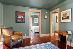 A room with a leather chair, a wooden desk, a blue floral rug, and a poster on the wall. - Cork Quarters | Historic Charm & Modern Comfort (Michigan City)