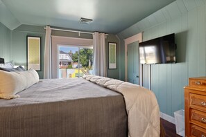 Ein Schlafzimmer mit Bett, Kommode, Fernseher und Blick ins Freie.