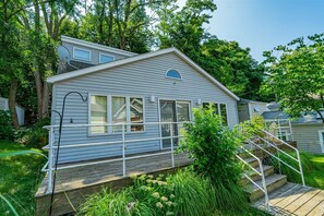 A single-story house with a deck, surrounded by lush greenery. - Down Time Cottage 1 Block to Lake Michigan Beaches (Michigan City)