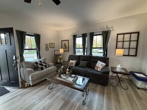 A furnished living room with a sofa, a coffee table, and a lamp. - Dragonfly in the Pines | Remodeled Forest Getaway (Michigan City)
