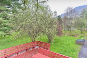 Eine Holzterrasse mit roter Geländer, die auf eine Wiese mit Bäumen und einem Berg im Hintergrund blickt.