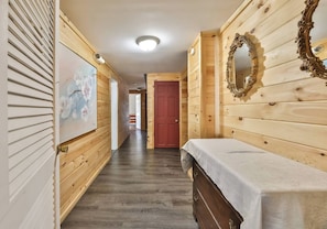 A hallway with wooden walls, a painting, a mirror, and a bed with a white cover. - 8Br 7Bath Sleeps 25+ Game hot tube 3 Min to MT (Hunter)