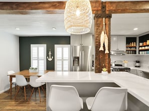 A modern kitchen with a large island, stainless steel appliances, and a hanging light fixture. - Dune Blast Cottage | Hot Tub, Fire Pit & Beach (Michigan City)
