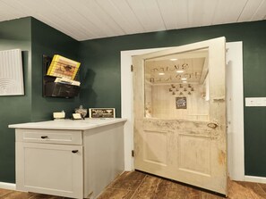 A room with a white cabinet, a door with a sign, and a wall-mounted shelf with items. - Dune Blast Cottage | Hot Tub, Fire Pit & Beach (Michigan City)
