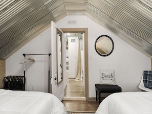 Een slaapkamer met twee bedden, een spiegel, een kussen met de tekst 'Beach' en een gang naar een badkamer.