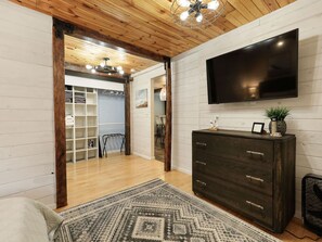 Een kamer met een houten plafond, een aan de muur bevestigde televisie, een donker houten dressoir en een kamerbreed tapijt met een patroon.