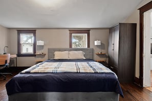 A bedroom with a large bed, two bedside tables with lamps, a desk, and a wardrobe. - The Gable at 409 | Craftsman Charm in Downtown (Michigan City)