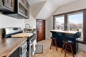 A kitchen with a stove, sink, and bar stools. - The Gable at 409 | Craftsman Charm in Downtown (Michigan City)
