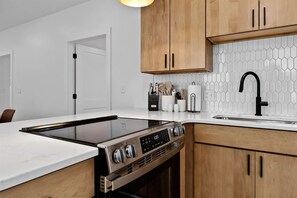 A modern kitchen with a built-in stove, wooden cabinets, a white countertop, and a hexagonal tile backsplash. - The Gingerbread Flat | Storybook Charm in Downtown (Michigan City)