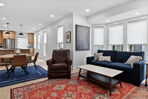 A modern living room with a blue sofa, a brown leather chair, and a coffee table. - The Gingerbread Flat | Storybook Charm in Downtown (Michigan City)
