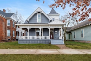 A two-story house with a porch, a chimney, and a small tower-like structure on the roof. - The Gingerbread Flat | Storybook Charm in Downtown (Michigan City)